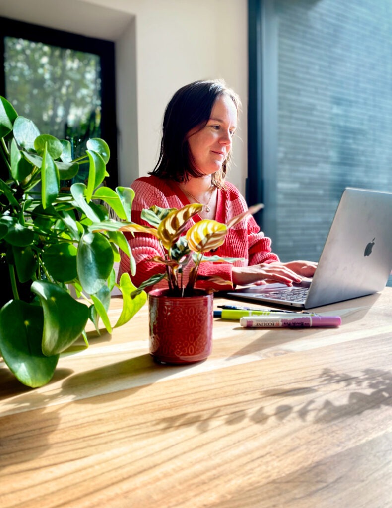 Sophie concentrée sur son travail, tapant sur son ordinateur portable. Son espace de bureau est visible, reflétant une ambiance créative et organisée.